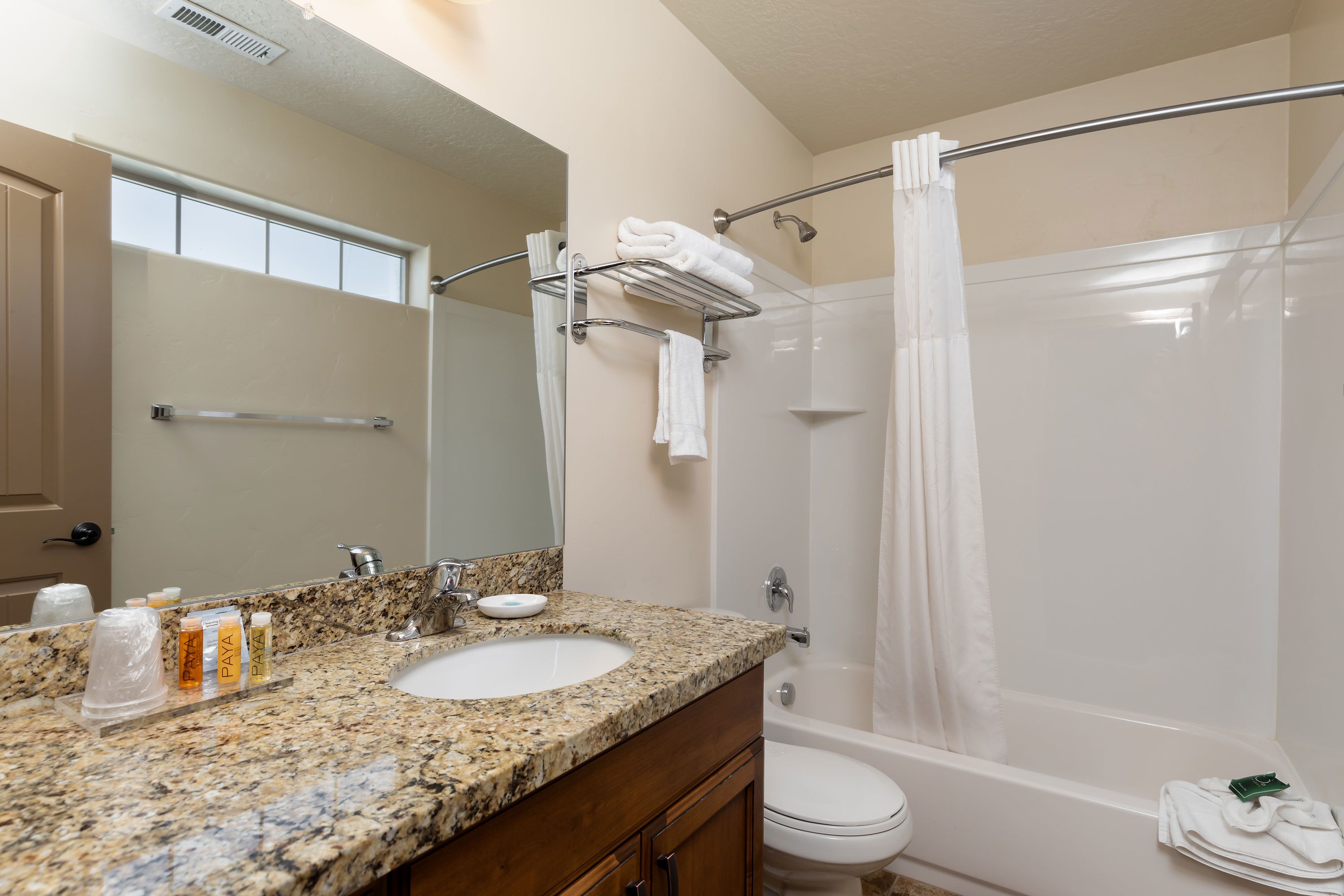 A bathroom with a granite countertop, a sink, a mirror, a toilet, and a shower with a glass door.