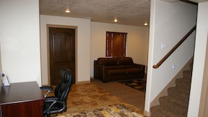 A home office with a desk, chair, and a brown leather couch. There is a staircase with carpeted steps and a patterned rug on the floor. - Duchesne Suites (Duchesne)