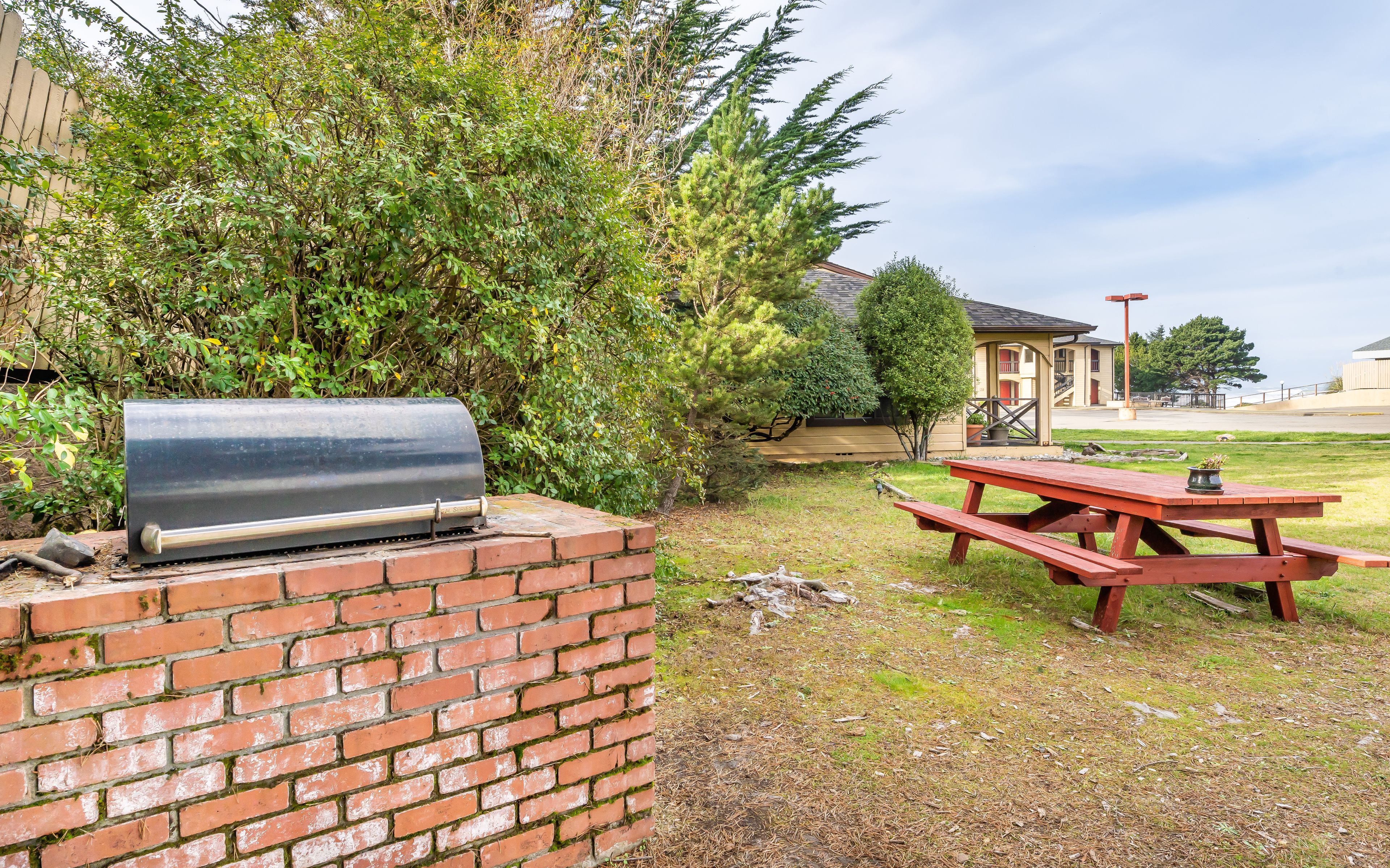 A brick barbecue grill, a picnic table, and a building in the background.