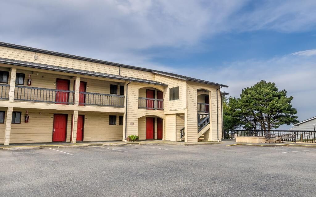 Un motel de varios pisos con techo plano, puertas rojas y estacionamiento.