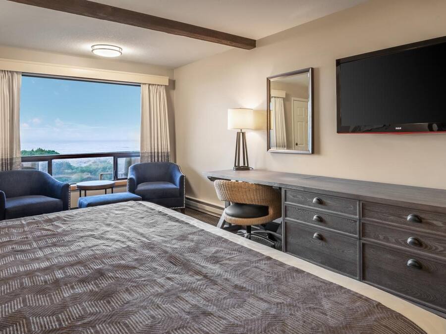 Une chambre d’hôtel avec un grand lit, deux fauteuils, un bureau avec une lampe, une télévision et une vue sur l’extérieur.