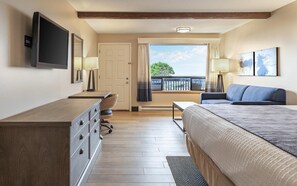 A hotel room with a bed, a desk, a chair, a TV, and a balcony with a view.