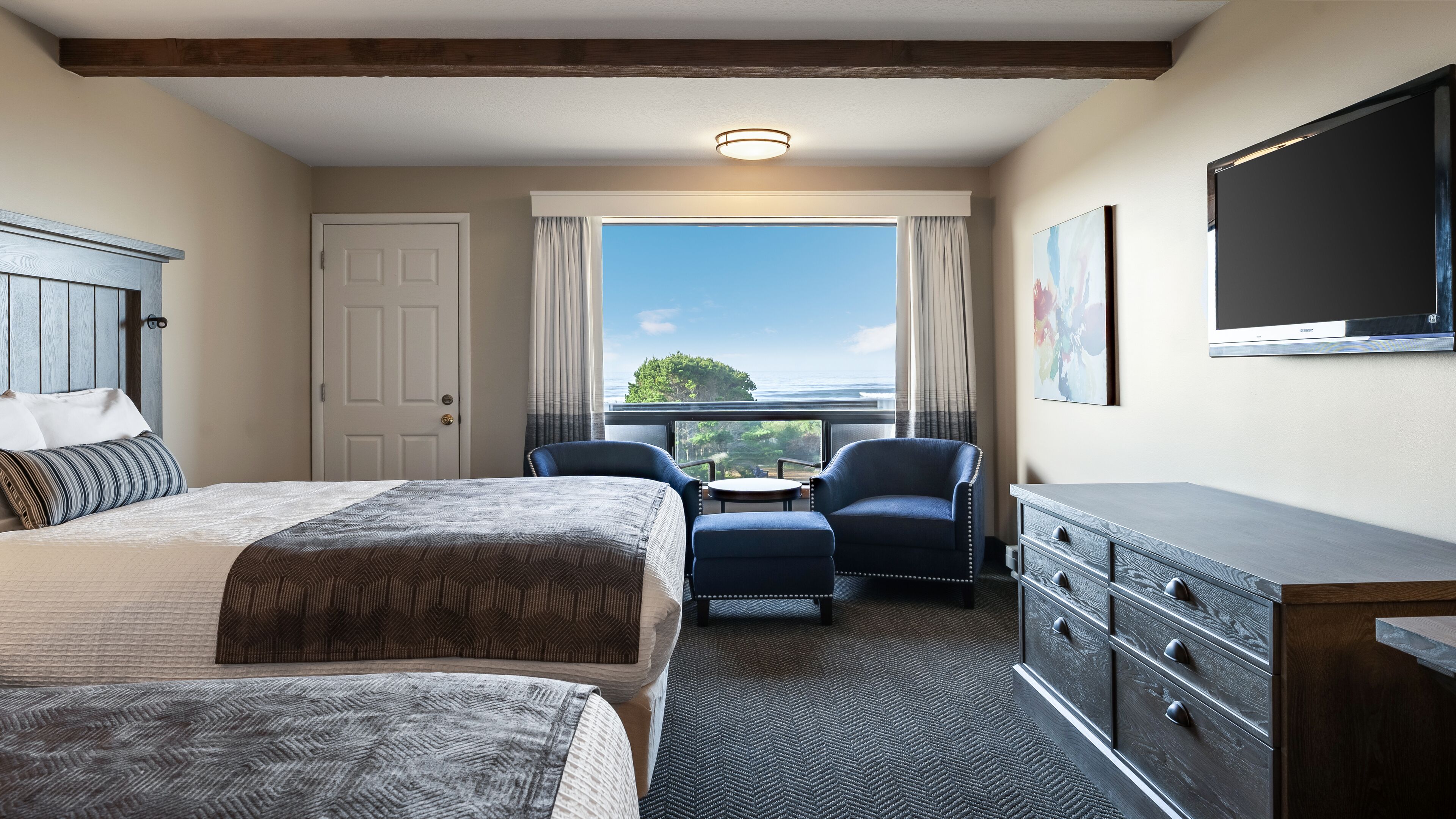 A hotel room with two beds, a desk, a chair, a dresser, and a television.