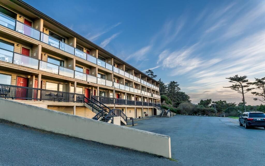 A multi-story motel with balconies, a parking lot, and a clear sky.