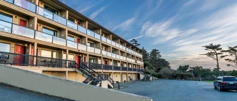 A multi-story motel with balconies, a parking lot, and a clear sky.