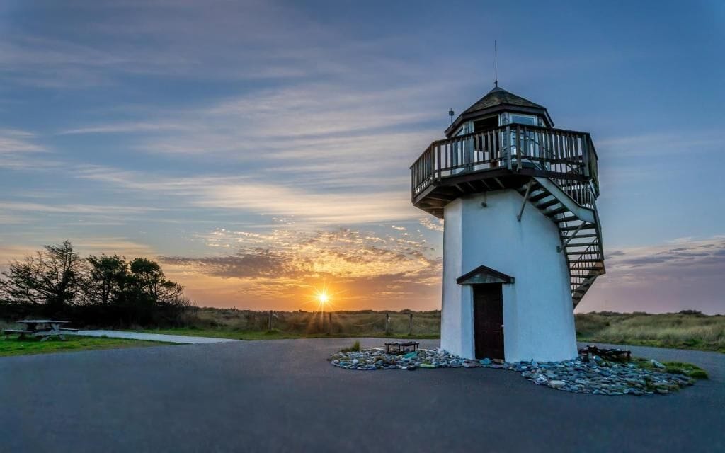 A solitary watchtower with a spiral staircase, a flat roof, and a small door, set against a sunset backdrop.