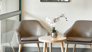 Dos sillones de cuero enfrentados, con una pequeña mesa redonda entre ellos, una orquídea en maceta sobre la mesa y un panel de vidrio a la izquierda.