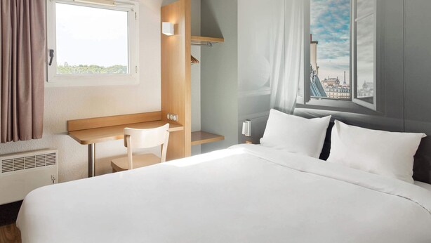 Habitación de hotel con cama, escritorio, silla y ventana que ofrece vistas a la ciudad.