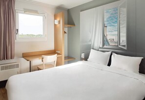 Habitación de hotel con cama, escritorio, silla y ventana que ofrece vistas a la ciudad.