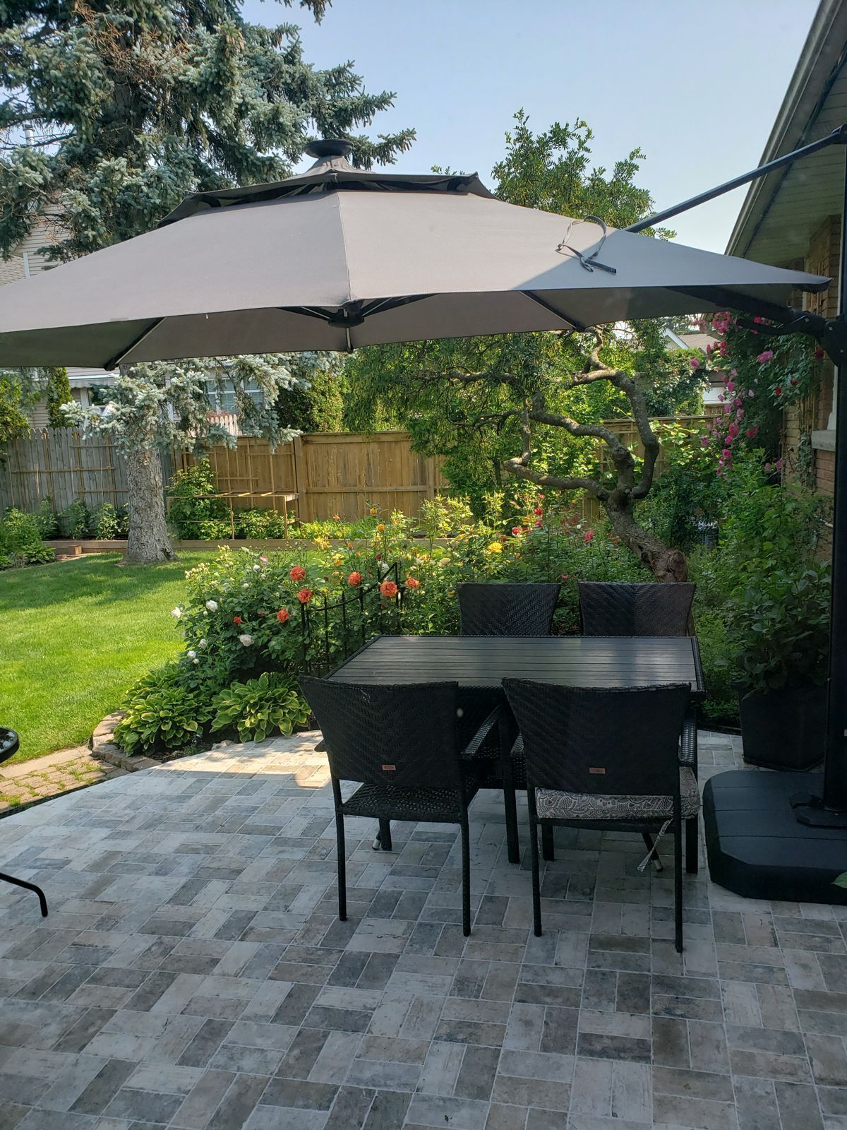 An outdoor patio with a table and chairs, a large umbrella, and a garden with various plants and flowers.