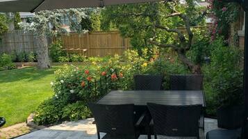 An outdoor patio with a table and chairs, a large umbrella, and a garden with various plants and flowers.