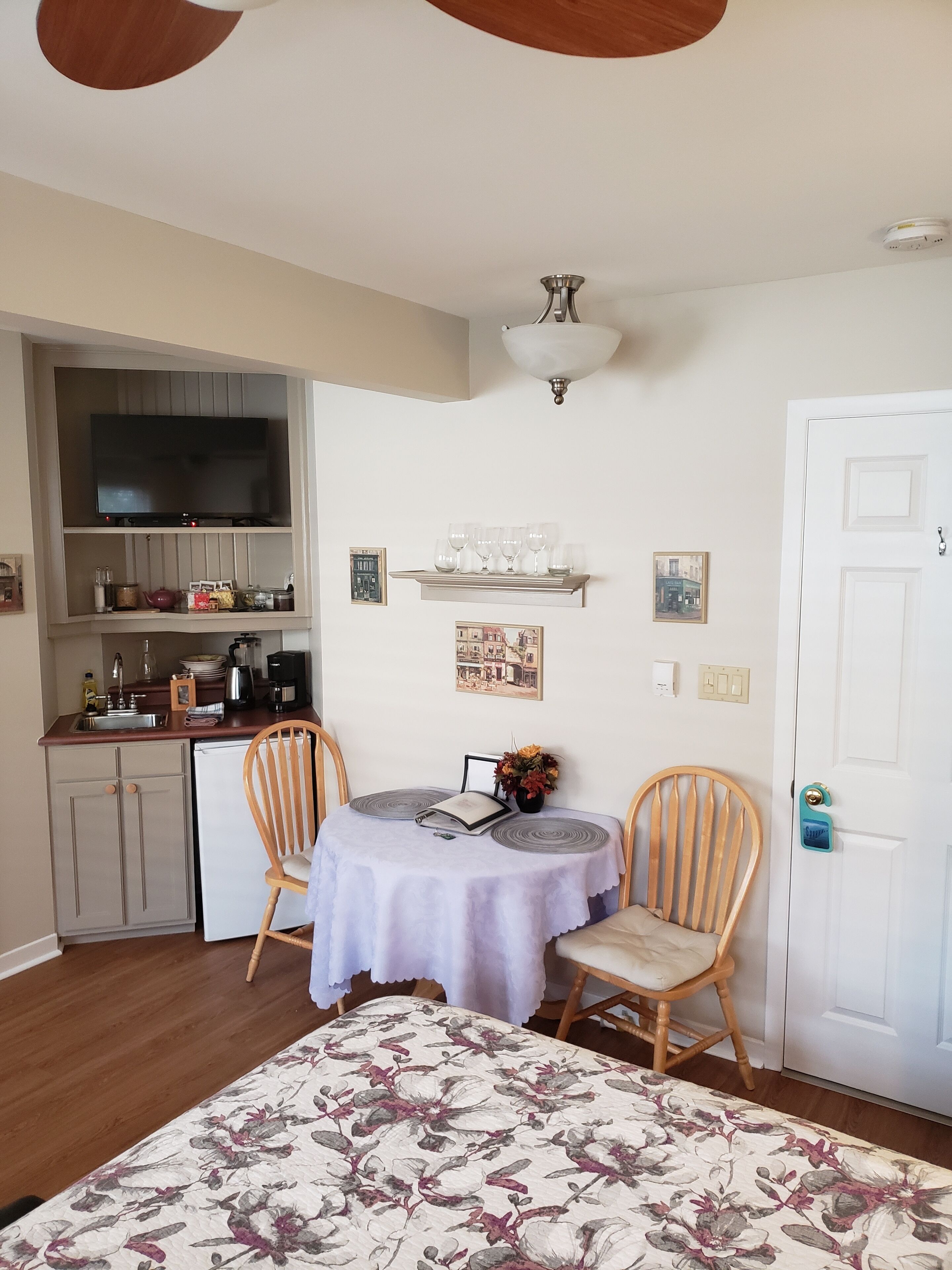 A compact living space with a kitchenette, a dining area with two chairs, a table with a book and a vase, and a ceiling fan.