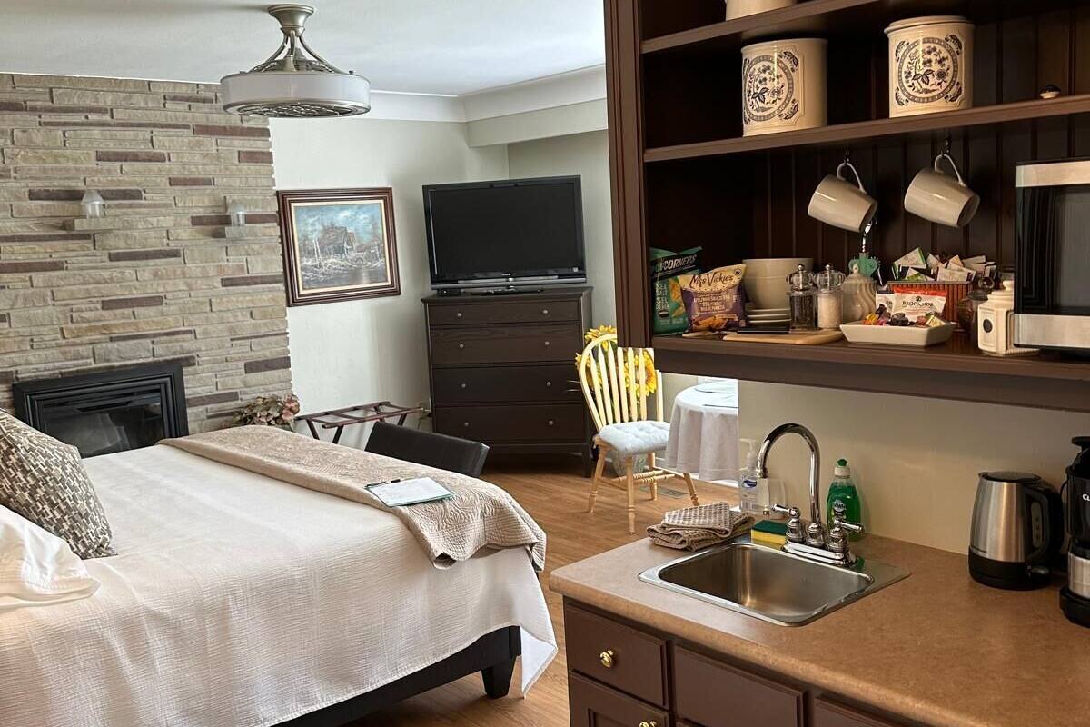 Une chambre à coucher comprenant un lit, une commode, un téléviseur et un coin cuisine avec un évier et des placards.
