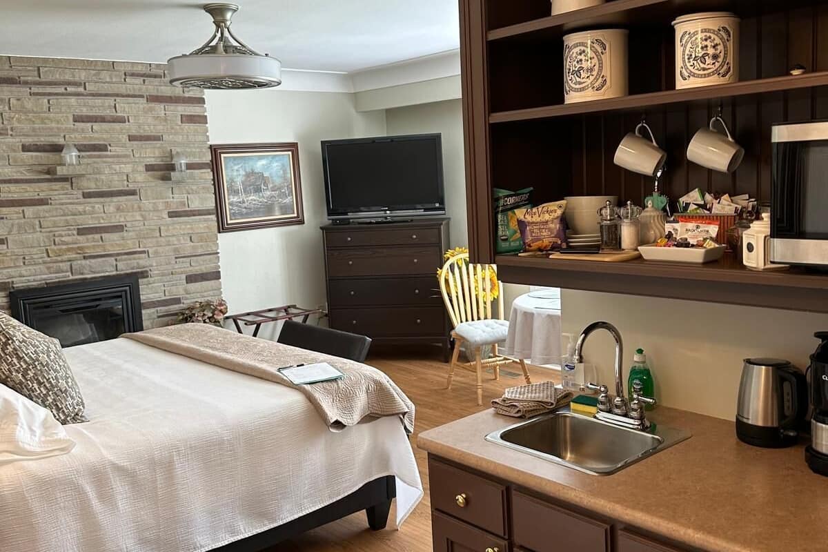Une chambre à coucher comprenant un lit, une commode, un téléviseur et un coin cuisine avec un évier et des placards.