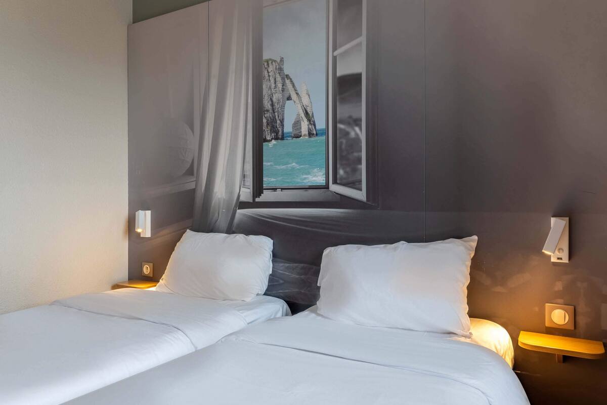 A hotel room with two beds, a large window with a view of a coastal rock formation, and bedside lamps.