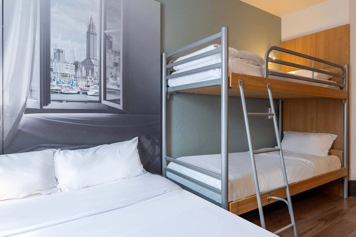 A bunk bed room with a cityscape view through a window, a bed with white linens, and a wooden headboard.