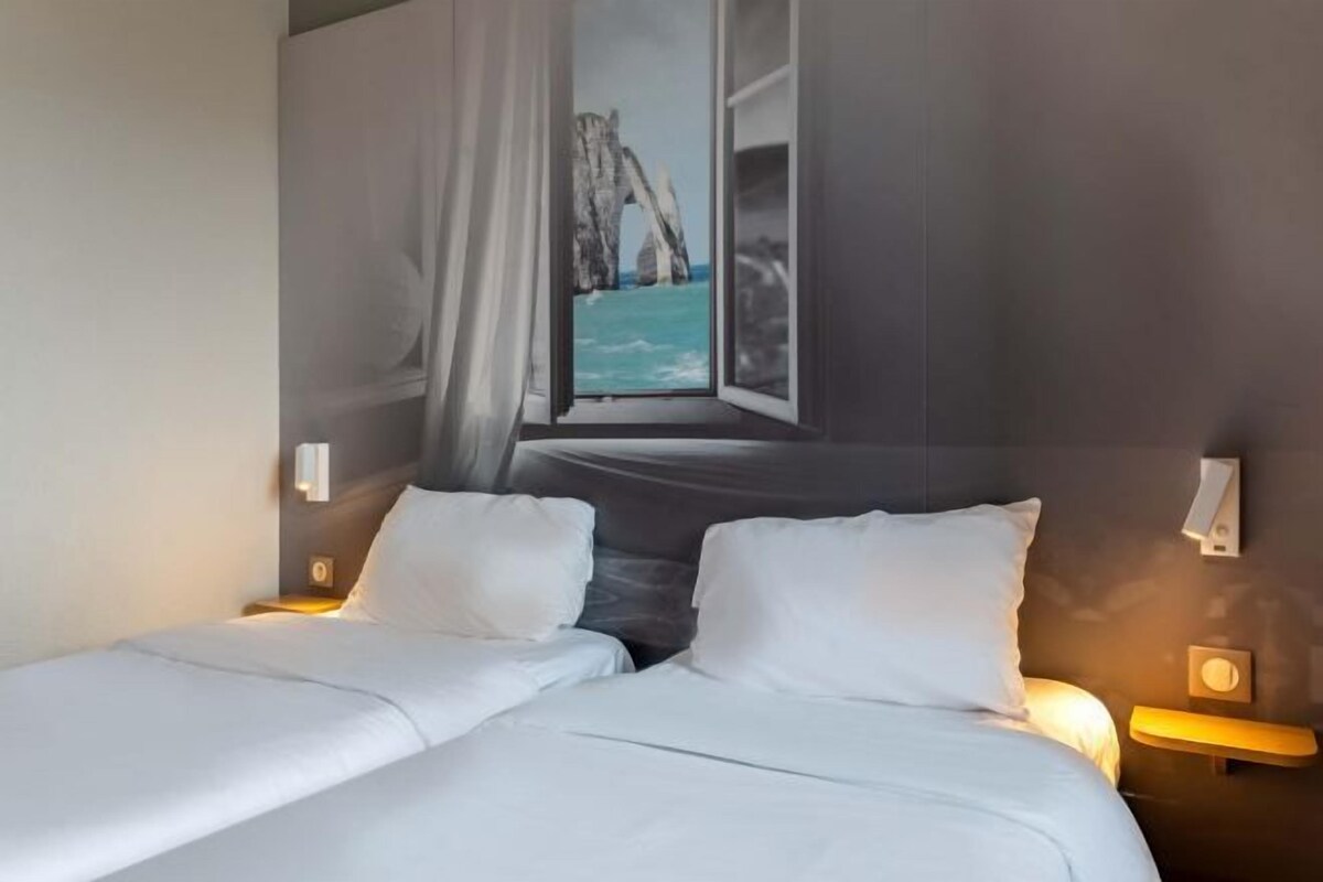 Una habitación de hotel con una cama, dos mesitas de noche y un ventanal con vistas a un paisaje costero.
