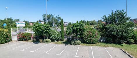 A parking lot with marked spaces, surrounded by greenery and a fence.
