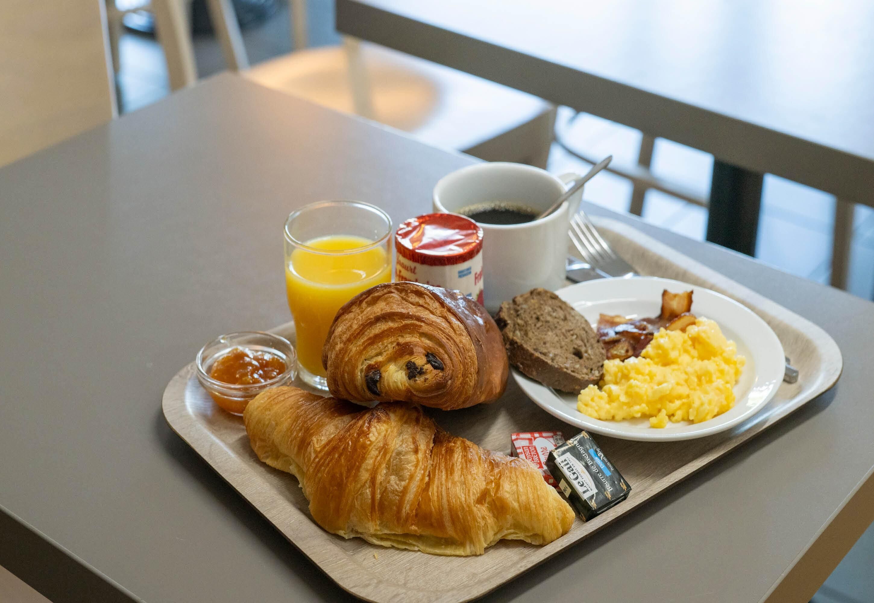 A breakfast tray with croissants, scrambled eggs, toast, orange juice, coffee, and jam.