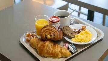 A breakfast tray with croissants, scrambled eggs, toast, orange juice, coffee, and jam.