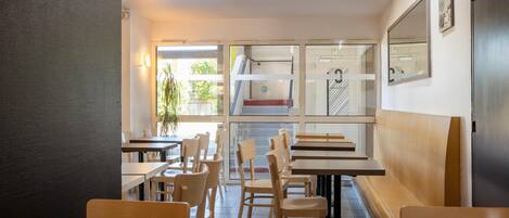 Interior de restaurante con mesas y sillas de madera, una escalera y ventanas amplias.