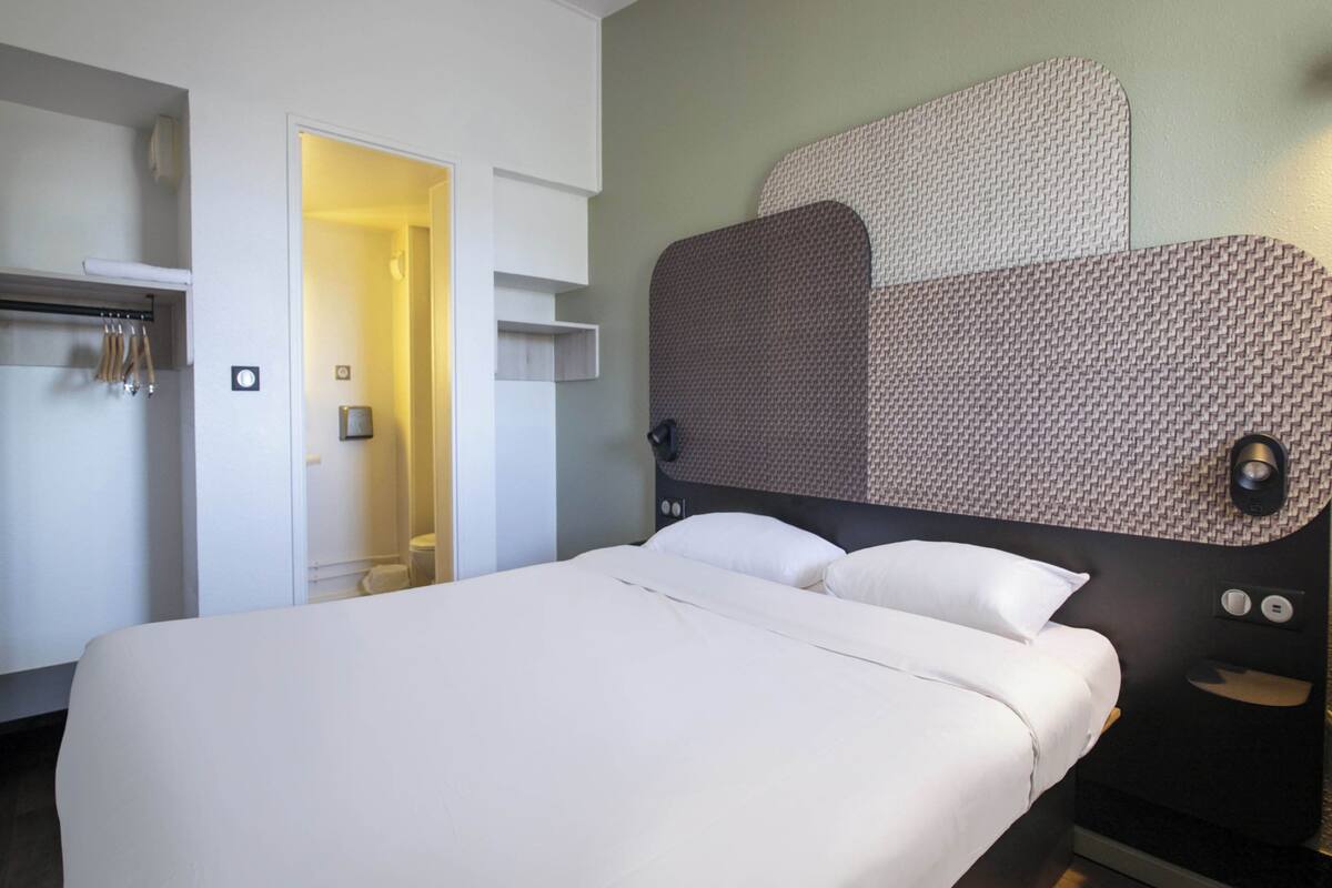 A hotel room with a large bed, a wardrobe, and a headboard with a textured design.