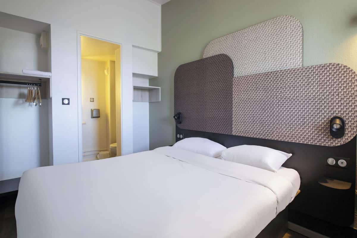 A hotel room with a bed, a wardrobe, a mirror, and a door leading to a bathroom.