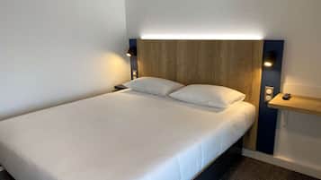 A neatly made bed with white linens, a wooden headboard, and two wall-mounted reading lights.