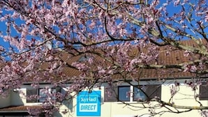 Un edificio con un letrero que dice "Kyriad DIRECT" y un estacionamiento con espacios demarcados.
