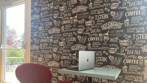 Una habitación con una laptop sobre una mesita, una silla roja y una pared negra con palabras relacionadas con comida y bebidas.