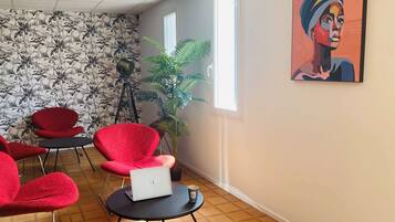 Een kamer met rode stoelen, een laptop, een plant en een schilderij aan de muur.