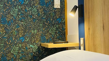 A hotel room with a bed, a nightstand, a wall clock, and a bedside lamp.