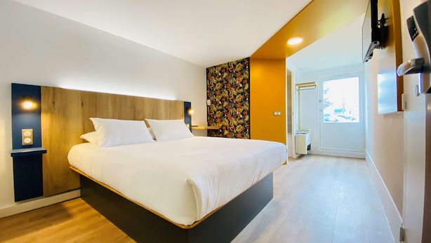 Una habitación de hotel moderna con una cama grande, cabecera de madera y una pared decorada con motivos florales.