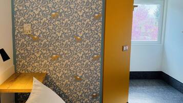 Hotelkamer met een bed, een klein tafeltje, een nachtkastje, een bloemenbehang en een raam en een deur.
