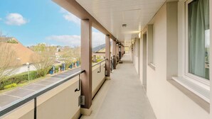Un couloir couvert donnant sur la rue, agrémenté d’une balustrade, de fenêtres et offrant une vue sur un ciel dégagé.
