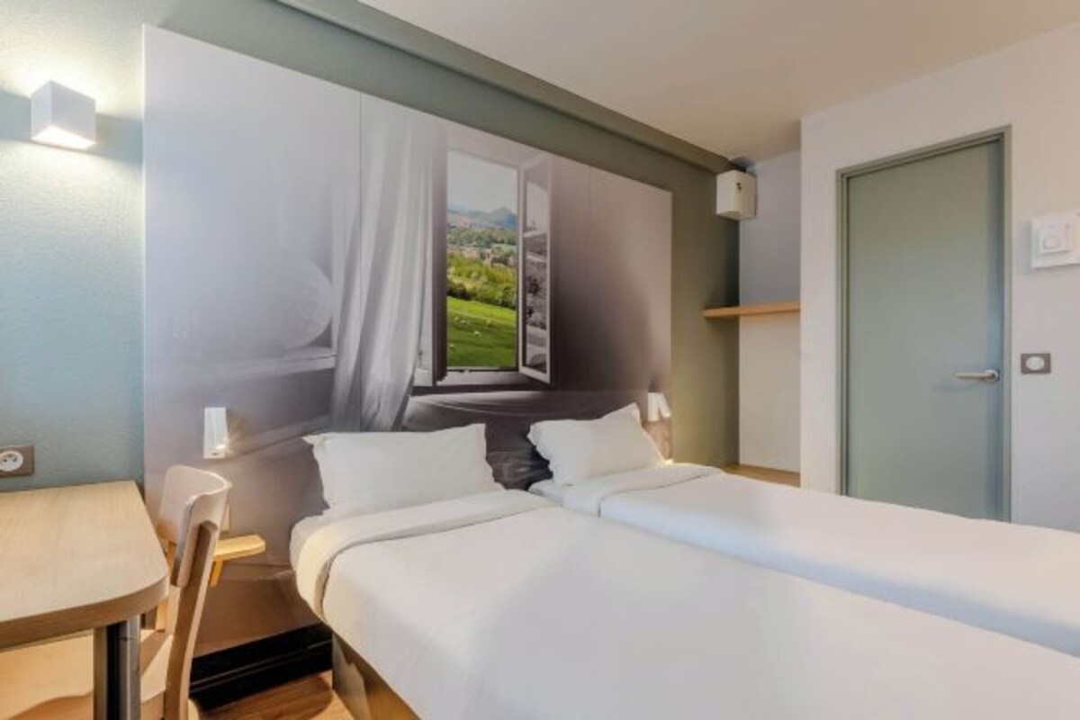 A hotel room with two beds, a window with a view, a desk, and a door.