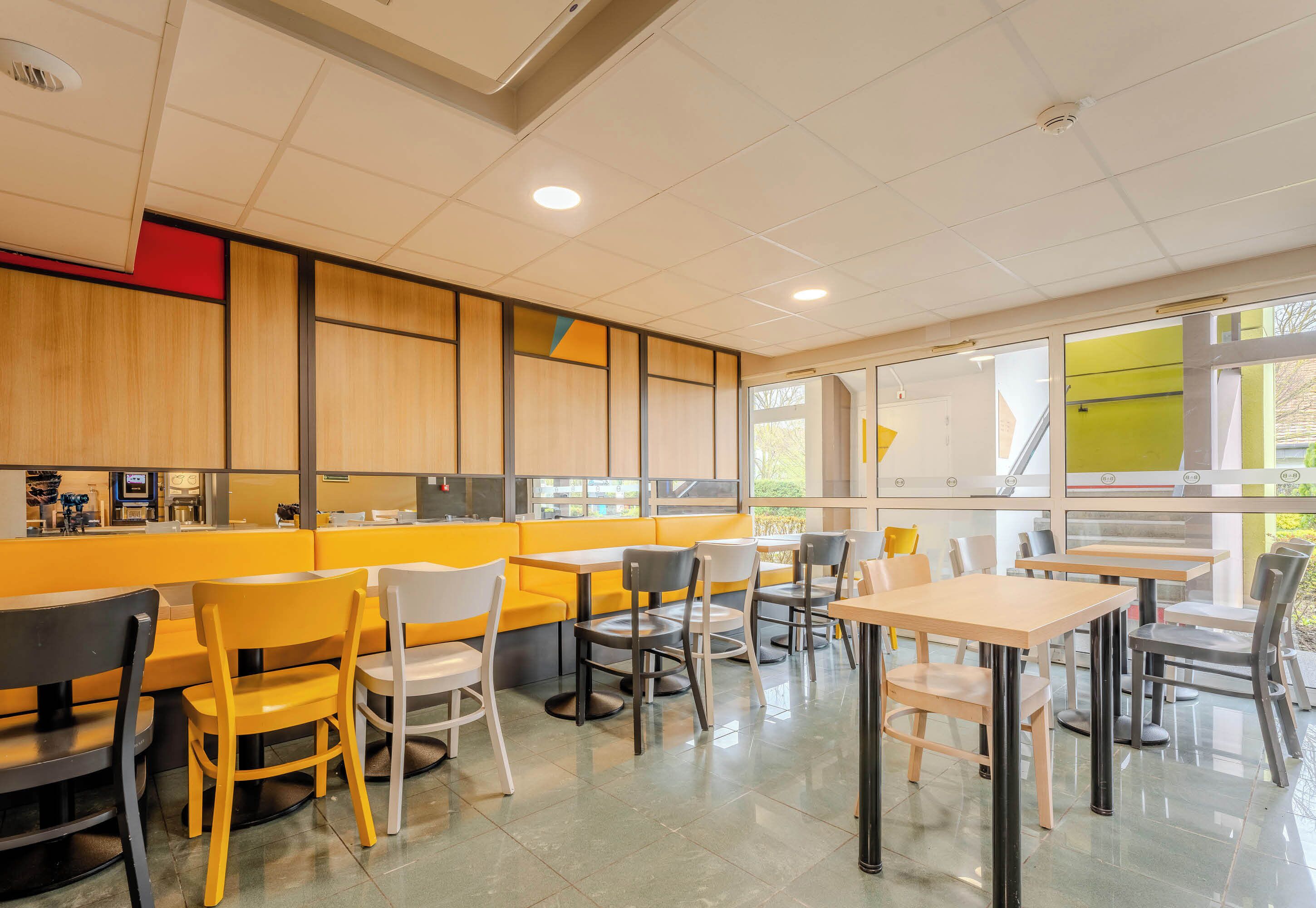 A modern restaurant interior with yellow and white seating, a counter, and large windows.