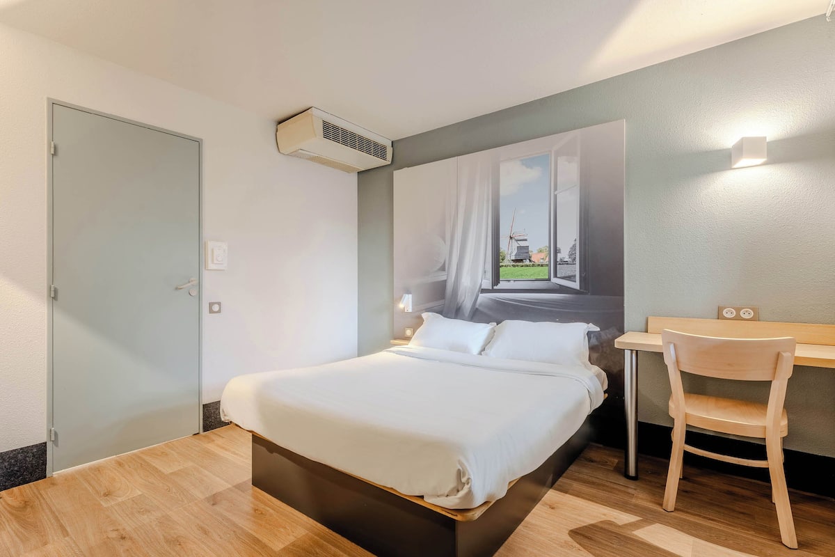 A modern hotel room with a large bed, a desk, and a chair.