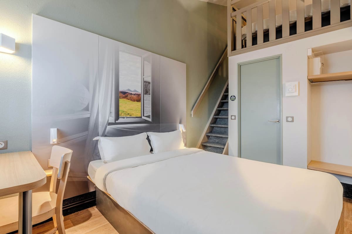 A bedroom with a bed, a desk, a chair, a staircase, and a door.