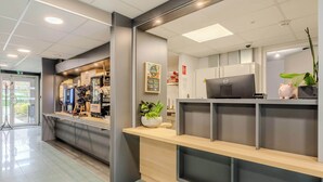 Un comptoir d’accueil avec un ordinateur, une plante et une caisse enregistreuse.
