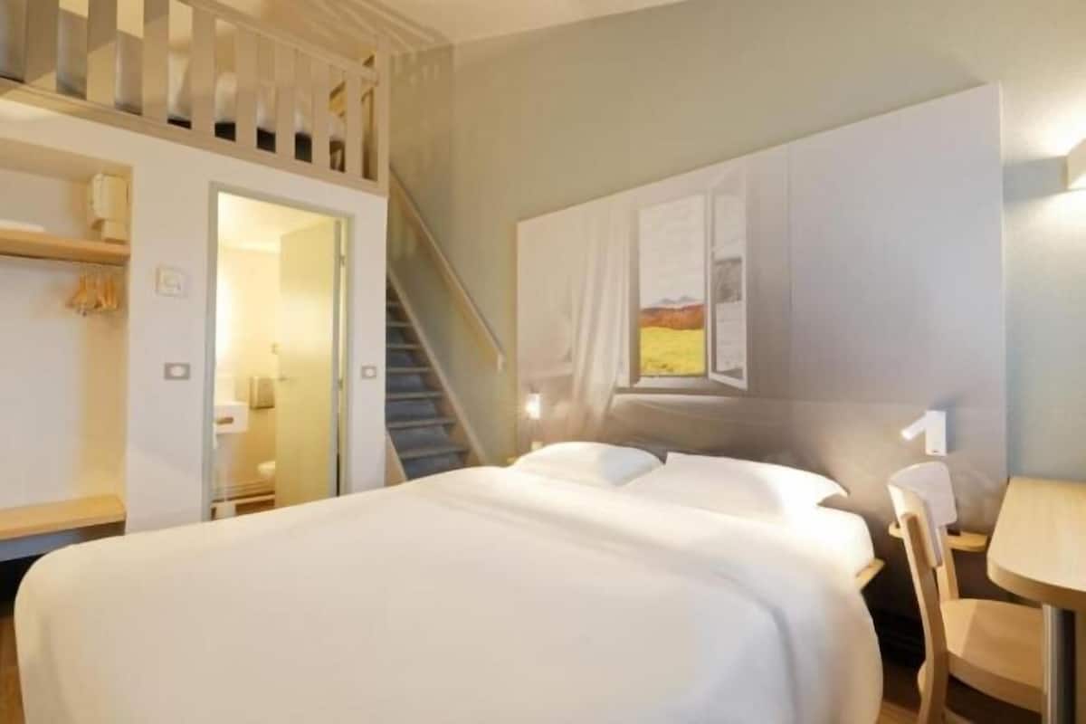 A hotel room with a bed, a desk, and a staircase leading to an upper level.