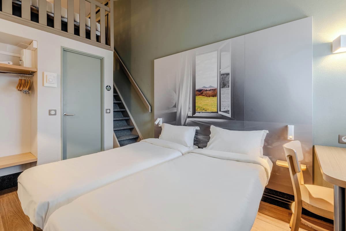 A hotel room with a bed, a desk, a chair, a wardrobe, and a staircase.