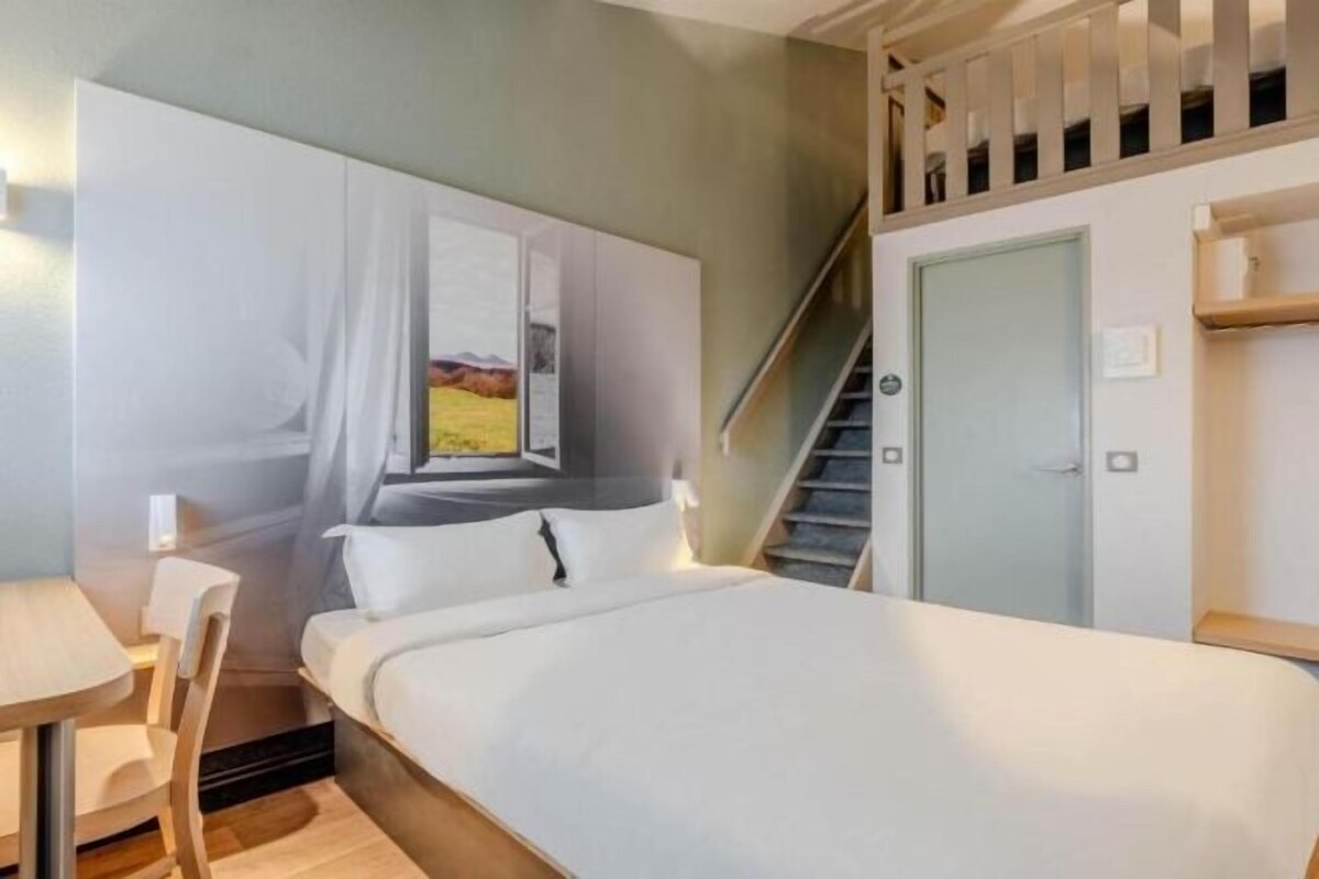 A bedroom with a bed, a desk, a chair, a staircase, and a door.