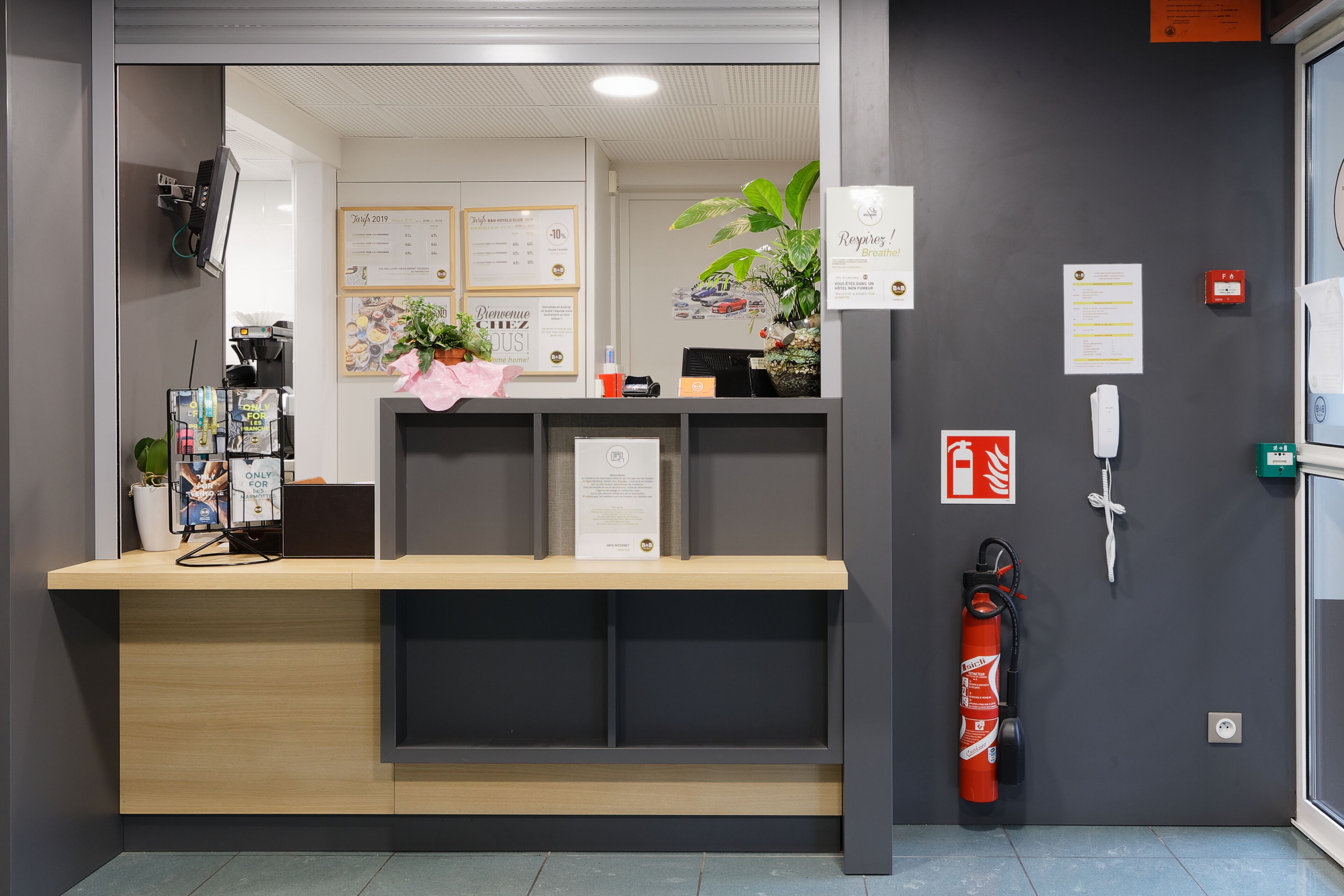 A reception desk with a wooden counter, a fire extinguisher, and various informational posters on the wall.