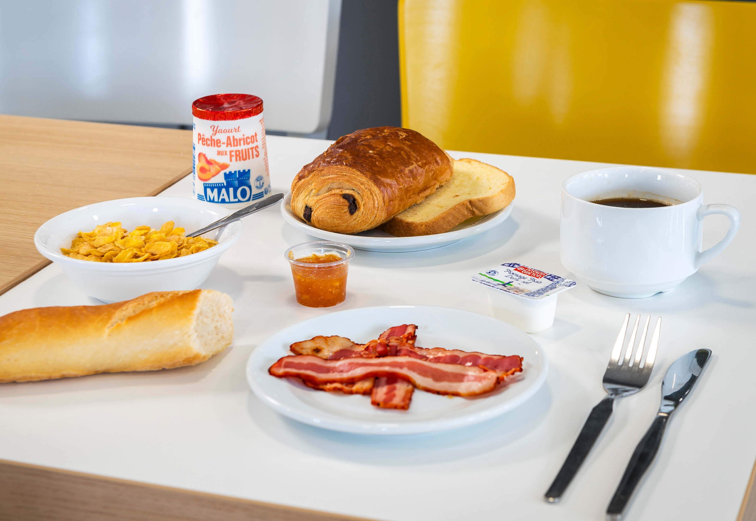 A breakfast tray with croissant, bacon, cereal, and coffee.