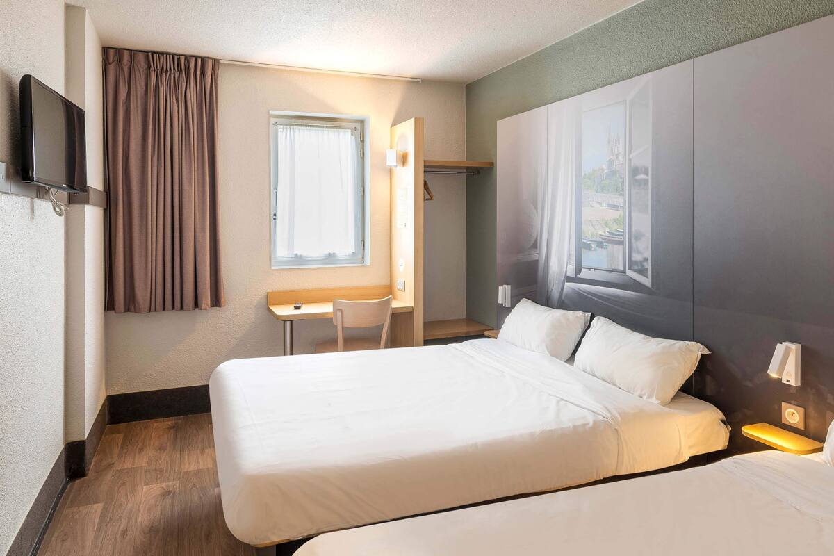 A hotel room with a bed, a desk, a chair, a TV, and a window with curtains.