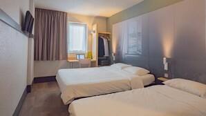Habitación de hotel con dos camas, un escritorio, una silla, perchero y televisión montada en la pared.