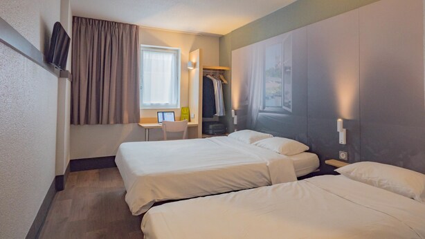 Habitación de hotel con dos camas, un escritorio, una silla, perchero y televisión montada en la pared.
