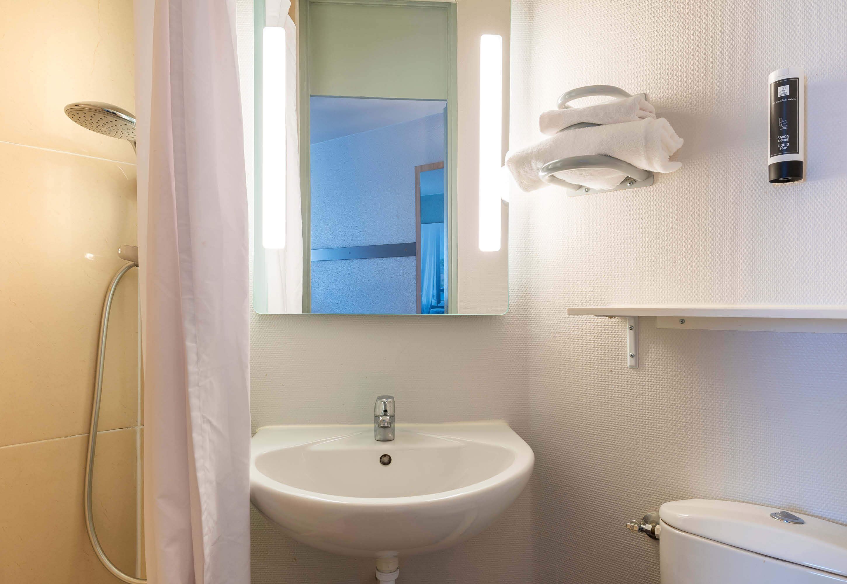 A bathroom with a white sink, a shower, a toilet, and a mirror.