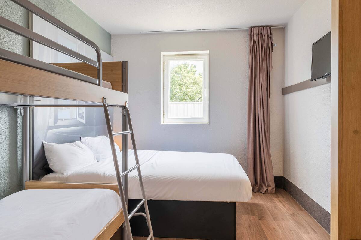 A room with bunk beds, a ladder, a window with a view, and a TV on the wall.